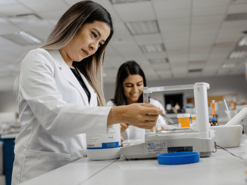 Two students in pharmacy lab, in white coats